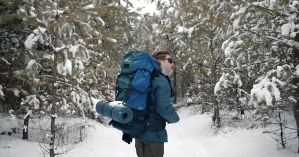 Бородатий пішохід з рюкзаком, що йде через зимовий ліс — стокове відео