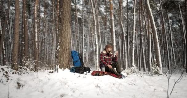 Wanderer sitzt im verschneiten Wald und trinkt Heißgetränk — Stockvideo