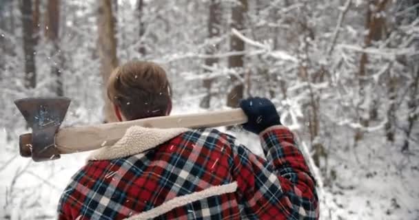 Back view of man with sharp axe in snowy forest — Αρχείο Βίντεο