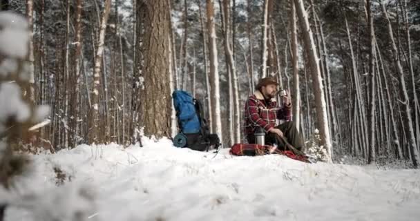 Mannelijke toerist die thee drinkt tijdens sneeuwval in het bos — Stockvideo