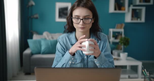 Attraktive Frau trinkt Kaffee und arbeitet am Laptop — Stockvideo