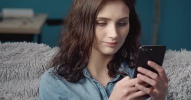 Mutlu bayan akıllı telefonuyla kanepede dinleniyor.