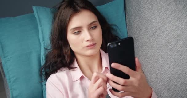 Retrato de menina bonita usando smartphone enquanto deitado no sofá — Vídeo de Stock