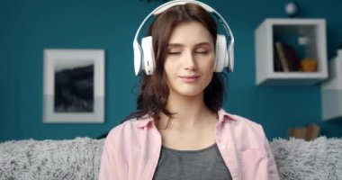 Kulaklıklı kız kanepede oturup müzik dinliyor.