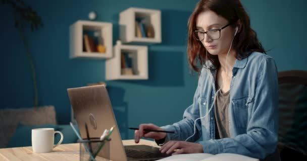 Молода дівчина в окулярах використовує ноутбук для навчання вдома — стокове відео