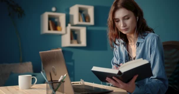 Señora seria estudiando en casa con portátil y libro — Vídeo de stock