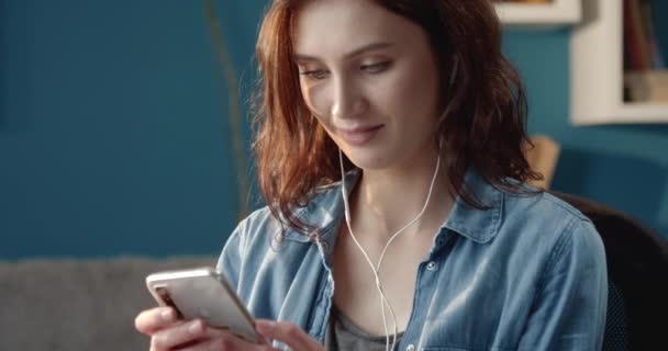 Счастливая молодая женщина сидит на диване и использует смартфон — стоковое видео