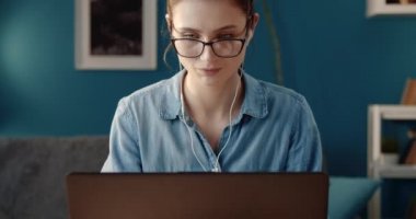 Gözlüklü mutlu kadın evde dizüstü bilgisayarla çalışıyor.