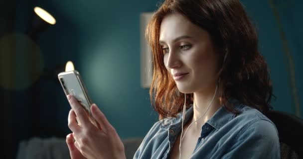 Улыбающаяся женщина пользуется смартфоном, сидя дома — стоковое видео