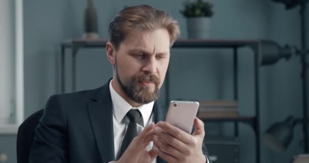 Уверенный человек сидит в офисе и пользуется смартфоном — стоковое видео