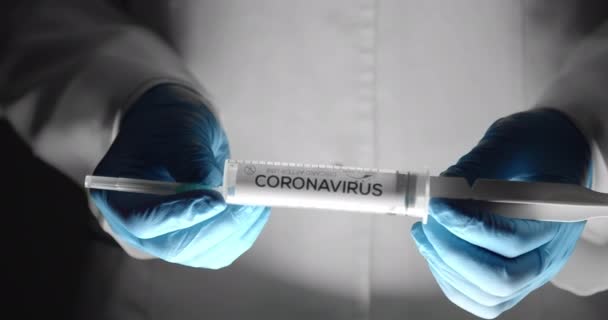 Lekarz w rękawiczkach trzymający strzykawkę z imieniem koronawirusa — Wideo stockowe