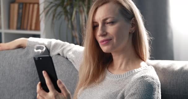 Šťastná žena relaxuje na gauči s chytrým telefonem — Stock video