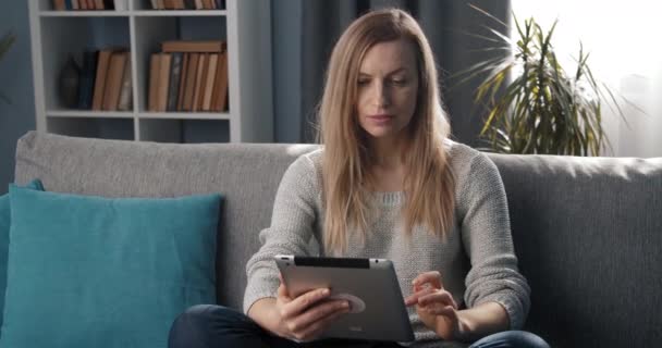 Senhora atraente usando tablet enquanto relaxa no sofá — Vídeo de Stock