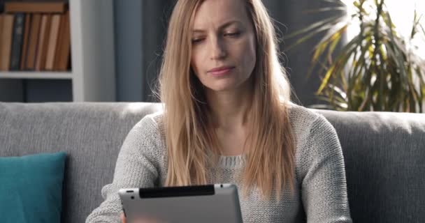 소파에 앉아서 디지털 기기를 만지고 있는 미소짓는 여성 — 비디오