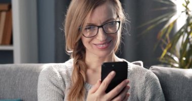 Kanepede dinlenirken akıllı telefon kullanan gülümseyen kadın.