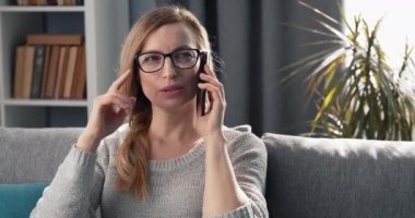 Güzel bir kadın kanepede oturuyor ve telefonla konuşuyor.