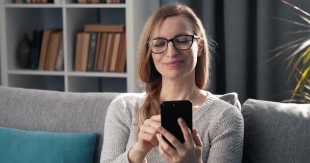 Glückliche Frau spricht im Wohnzimmer auf Smartphone — Stockvideo