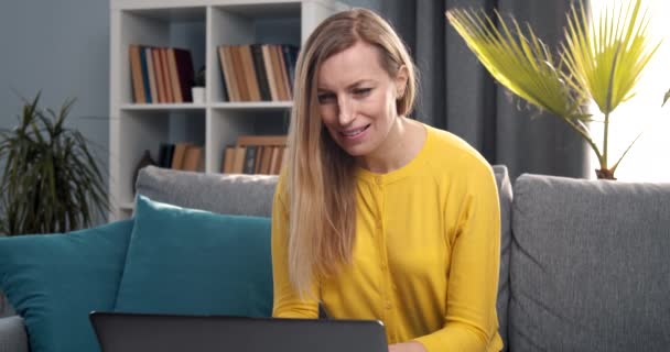 Mujer alegre sentada en el sofá y trabajando en el ordenador portátil — Vídeos de Stock