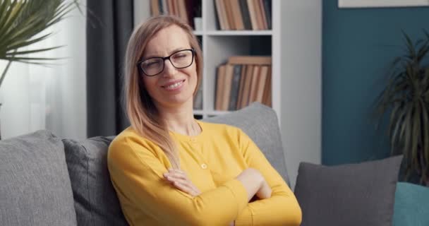 Nő sárga pulóverben és szemüvegben ül a kanapén — Stock videók