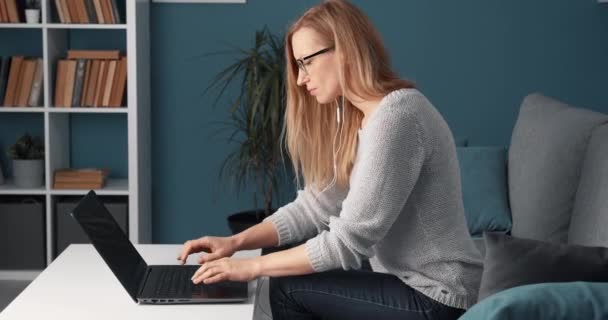Žena na volné noze pracuje na notebooku, zatímco sedí na gauči — Stock video