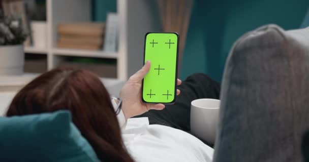 Woman relaxing on couch and holding phone with green screen — Stock Video