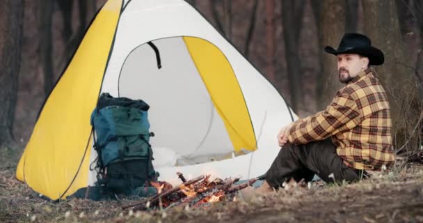 Mann rastet neben Zelt und Feuer im Wald aus — Stockvideo