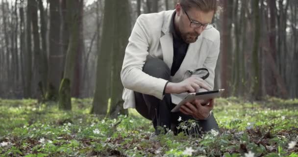 Зрелый ботаник, открывающий растения с лупой и планшетом — стоковое видео