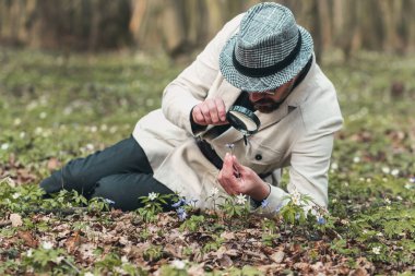 Büyüteçle çiçek inceleyen adam.