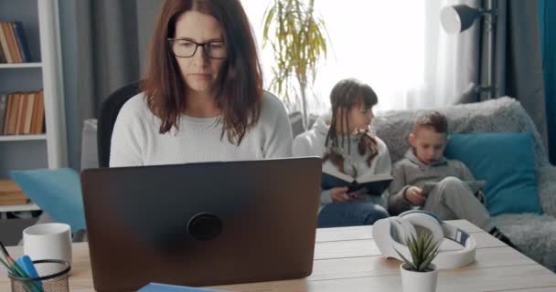 Dojrzała kobieta pracuje na laptopie i wychowuje swoje dzieci — Wideo stockowe