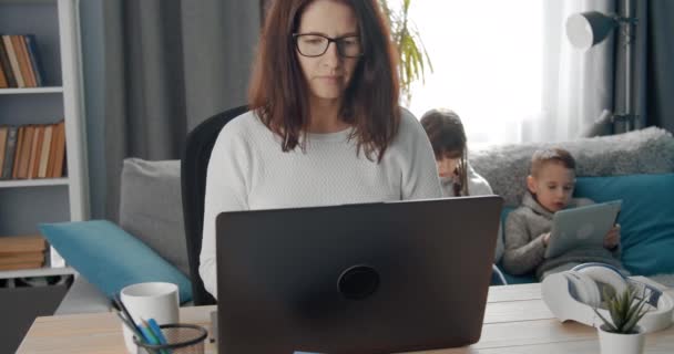 Magabiztos hölgy szemüveg dolgozik laptop gyerekekkel — Stock videók