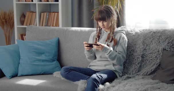 Menina muito adolescente relaxante no sofá com smartphone — Vídeo de Stock