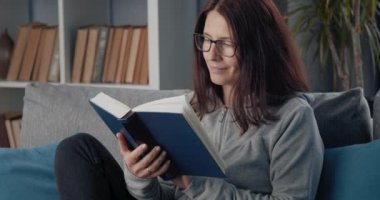 Rahat bir kadın kanepede oturup kitap okuyor.