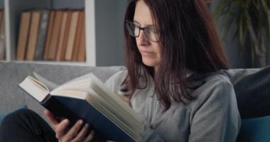 Gözlüklü mutlu kadın evde kitap okuyor.