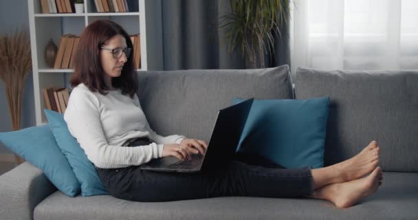 成熟女人躺在沙发上用笔记本电脑的侧视图 — 图库视频影像