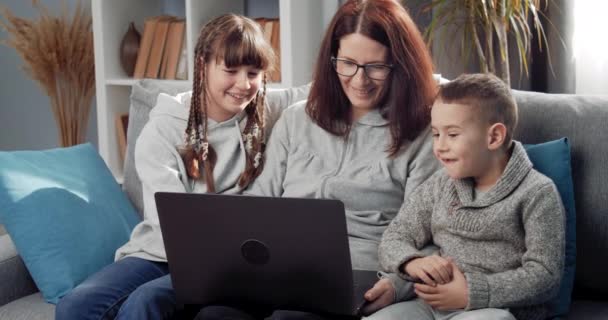 Lachende moeder en kinderen ontspannen op de bank met laptop — Stockvideo