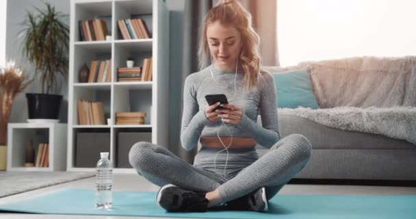 Menina ativa com smartphone e fones de ouvido relaxante em casa — Vídeo de Stock