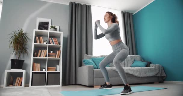 Активна чарівна жінка присідає, стоячи на килимку для йоги — стокове відео