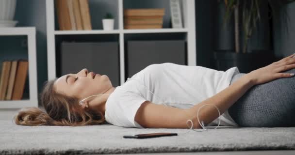 Menina cansada relaxando em fones de ouvido após o exercício da manhã — Vídeo de Stock