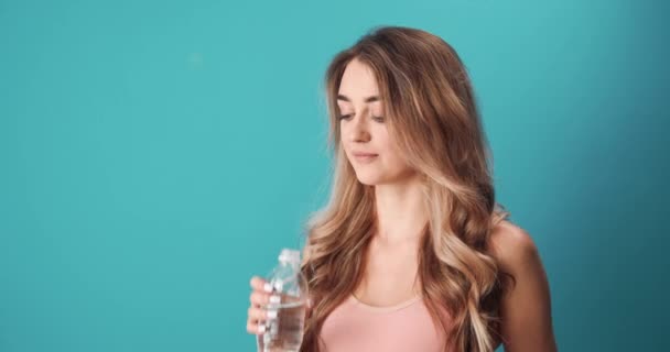 Спортивна жінка п'є воду на синьому фоні — стокове відео
