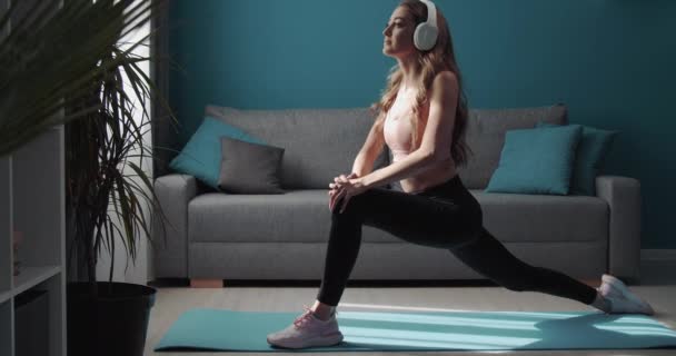 Menina forte em fones de ouvido alongando o corpo no tapete de ioga — Vídeo de Stock