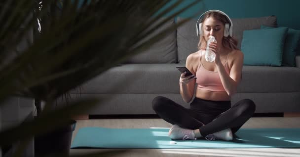 Женщина расслабляется на коврике для йоги после тренировки со смартфоном — стоковое видео