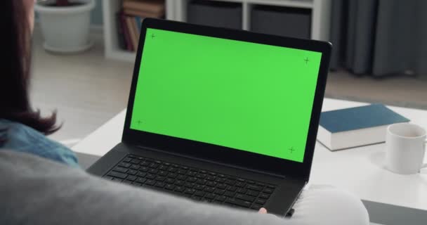 Chica sentada en casa con el ordenador portátil y mirando la pantalla verde — Vídeo de stock
