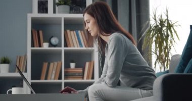 Kanepede oturan ve dizüstü bilgisayarla çalışan kadının yan görüntüsü.