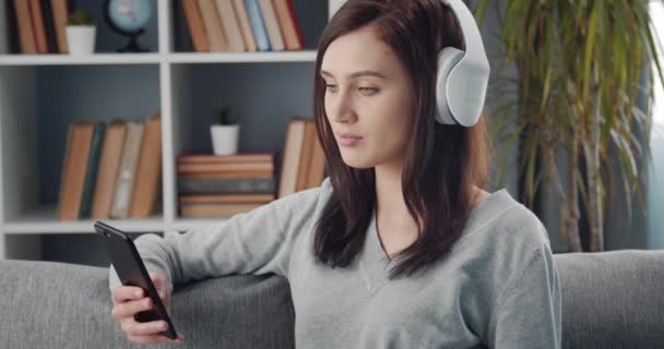 Girl sitting at home in headphones and looking at camera — Stock Video