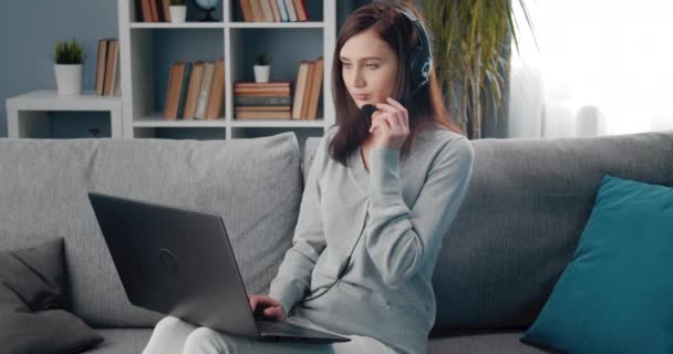 Mujer encantadora usando el ordenador portátil y auriculares para la videoconferencia — Vídeo de stock