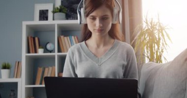 Kulaklıklı genç kız evde bilgisayar kullanıyor.