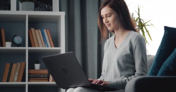 Mädchen entspannt sich auf Couch mit Kopfhörer und arbeitet am Laptop — Stockvideo