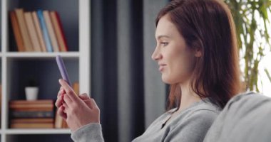 Mutlu kadın kanepede dinleniyor ve akıllı telefon kullanıyor.