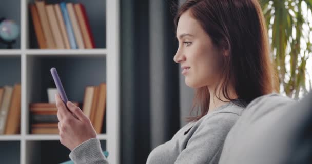 Aantrekkelijke vrouw met smartphone terwijl ze op de bank zit — Stockvideo