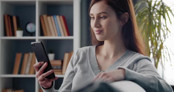 Señora feliz sentado en el sofá y el uso de un teléfono inteligente moderno — Vídeos de Stock